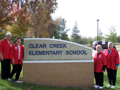 Photo of volunteer grandparents standing by the Clear Creek Elementary sign